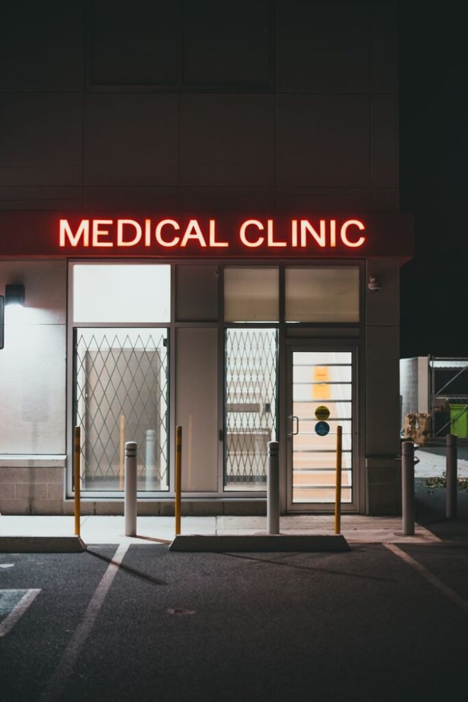 Night view of a medical clinic entrance illuminated by a neon sign in an empty parking area.