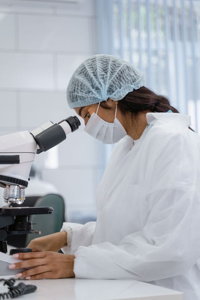 Female scientist examining samples with a microscope in a lab environment.